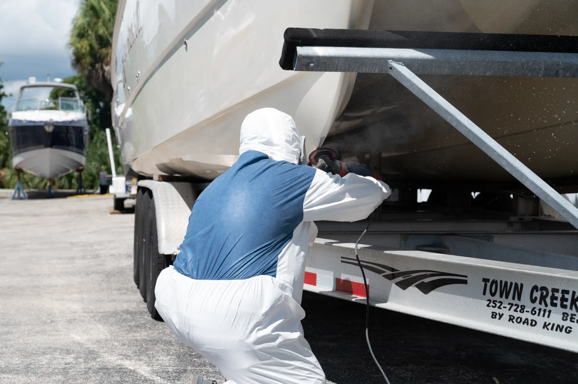 Boat Guys technician in a suit sanding a hull on the trailer